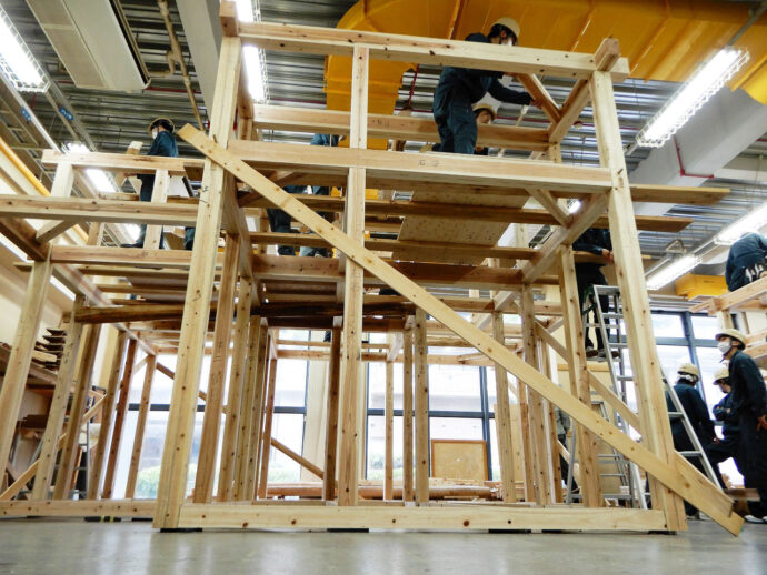 Wooden framing of a building under construction with workers wearing hard hats on the upper level.