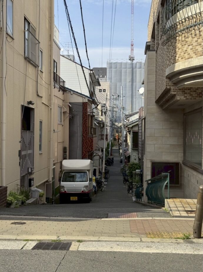 Narrow urban alley flanked by beige buildings, a small truck parked on the left, overhead power lines.